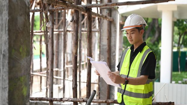 Engineer manager wearing safety vest and helmet standing at construction site.