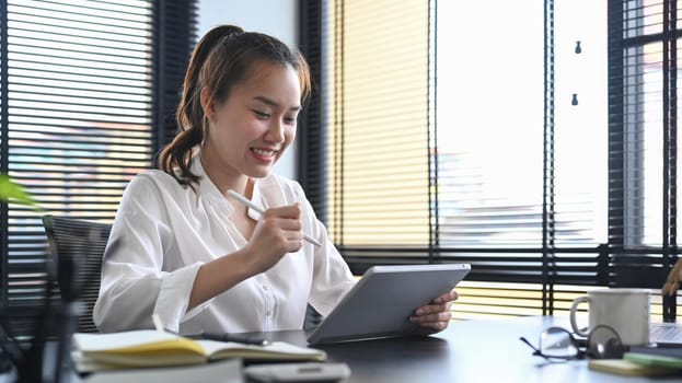 Young female office worker sitting in modern office and using digital tablet.