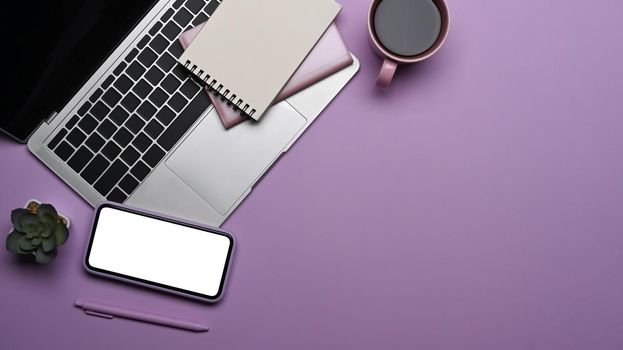 Smartphone with white screen laptop computer, coffee cup and notebook on purple background. Flat lay.