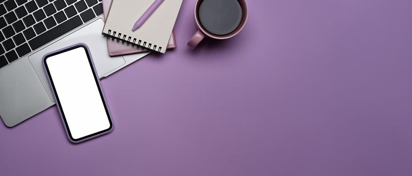 Mobile phone with empty screen, laptop computer, coffee cup and notebook on purple background. Top view.