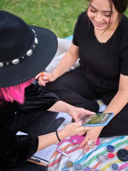 two young women looking at a design to characterize on the phone, sitting in the park