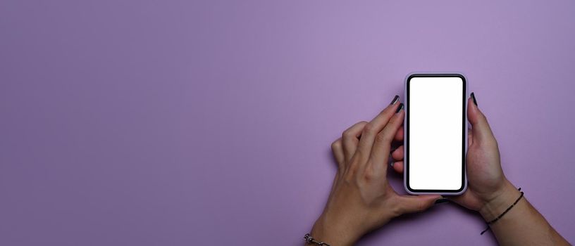 Young woman hands using smart phone with blank screen on purple background with copy space. Top view.