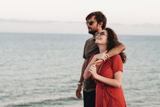 Portrait of Young Couple on Background of Sea, Happy Man Hugging Curly Woman in Red Dress at Sunset