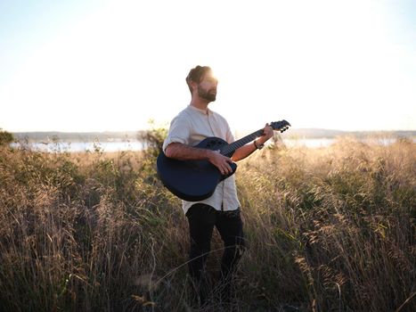 guitarist posing with his guitar in the countryside during sunset, horizontal portrait