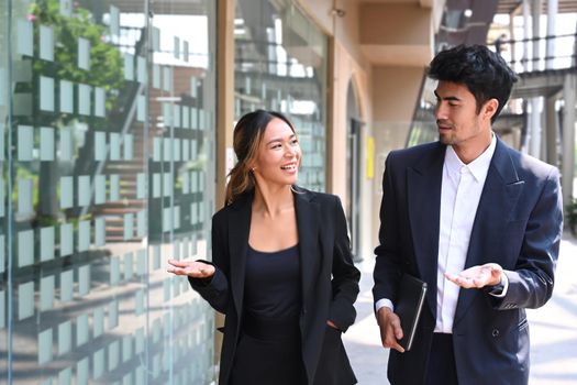 Handsome male business leader and his assistant talking to each other while walking outdoors.