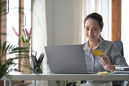 Charming woman holding credit card and shopping online on laptop computer.