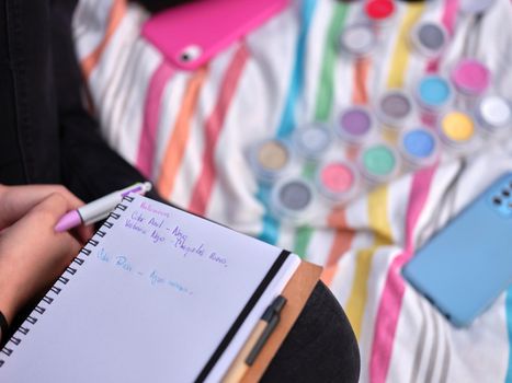Close-up of a girl's notebook with notes on possible make-ups, paints and a colorful striped blanket in the background