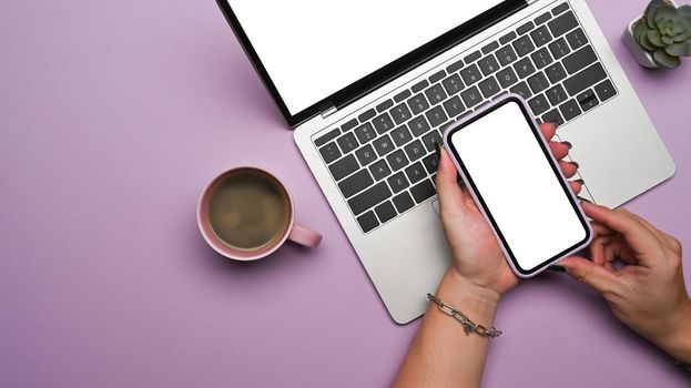 Woman using smart phone and laptop computer on purple background. Top view.