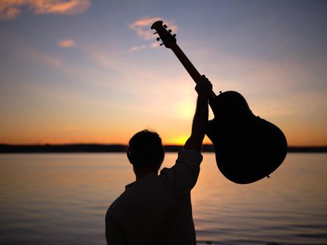 waist up silhouette of a man with his guitar held high watching the sundown on the pink lake, horizontal scenery background