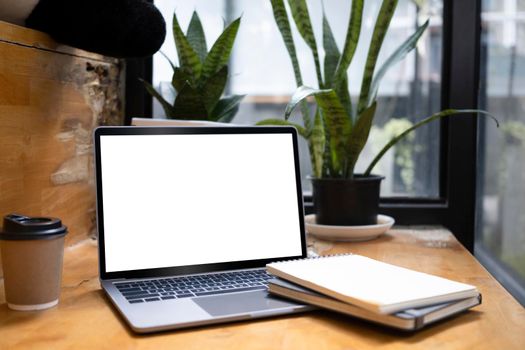 Comfortable workplace with laptop, notebook, coffee cup and house plat on wooden table.