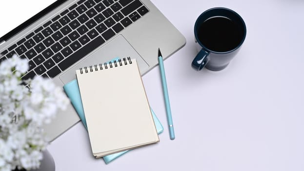 Empty notepad, laptop computer and coffee cup on white office desk. Top view.