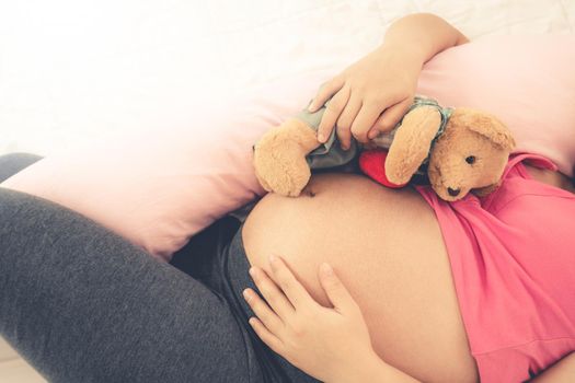 Happy pregnant woman sleeping on bed in bedroom at home for resting and stress relief. The young expecting mother holding baby in pregnant belly. Maternity prenatal care and woman pregnancy concept.