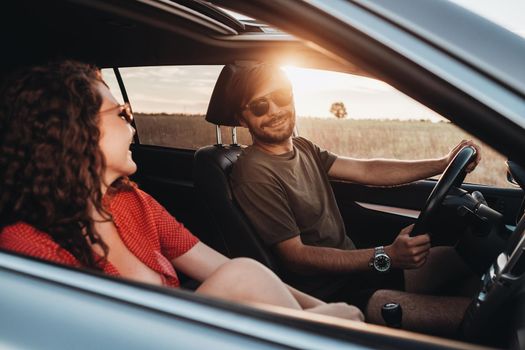 Cheerful Man and Curly Brunette Woman Sitting in Car, Young Couple Enjoying Road Trip at Sunset