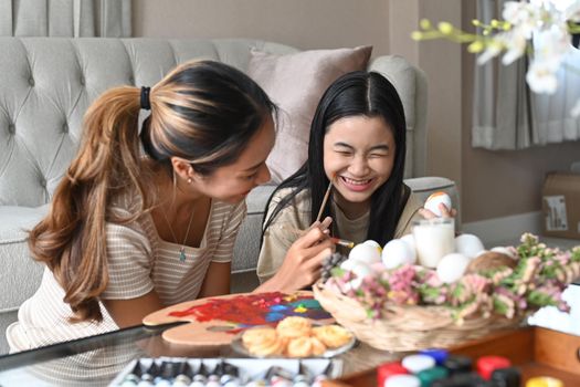 Mother drawing her daughter face while painting Easter eggs together.