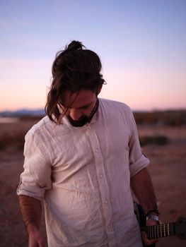 musician in a shirt facing the ground and with a guitar in his hand, vertical background in nature