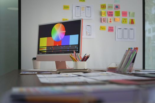 Creative designer workplace with computer pc, stationery and color swatches on wooden table.