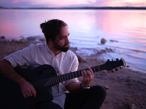 guitarist sitting by a lake reflecting the pink sunset light, horizontal close up, scenery background