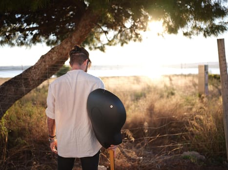 man on his back with guitar in hand looking down with the sunset in the background