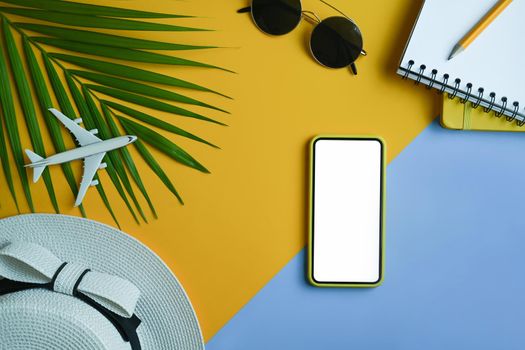 Flat lay smart phone, hat, notebook, sunglasses and tropical palm leaves on yellow background. Summer vacation concept.