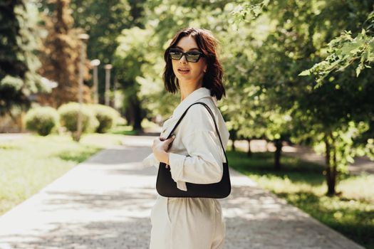 Portrait of Stylish Brunette Woman in Sunglasses with Hand Bag Outdoors at Sunny Summer Day