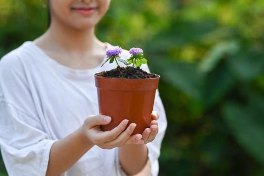 Smiling asian girl holding potted plant in hands against blurred green nature background on a sunny day. Earth day, Ecology concept.