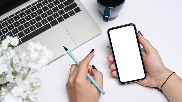 Mockup image of young woman sitting in front of laptop computer and using mobile phone.