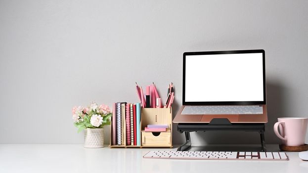 Home office desk with computer laptop, flower pot and coffee cup on white table.