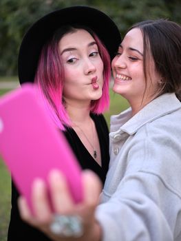 two friends having fun taking a selfie doing lip gestures, one with pink hair, vertical close up