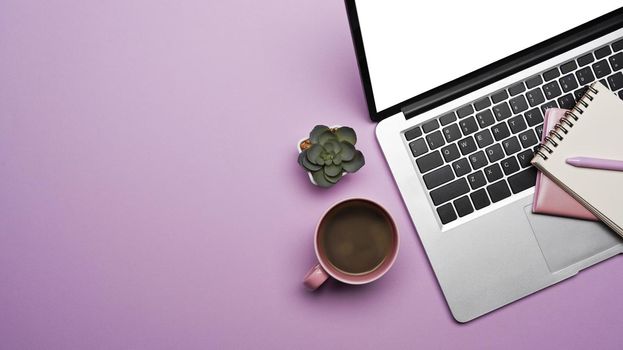 Top view laptop computer, coffee cup and notebook on purple background with copy space.