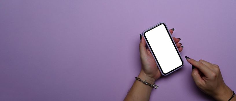 Woman hands using mobile phone with empty screen isolated on purple background. Top view.