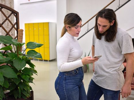 woman standing with mobile phone in hand showing her work to a co-worker, people on one side, horizontal