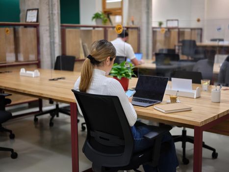 woman with her mobile phone sitting in a coworking space with other people, horizontal picture