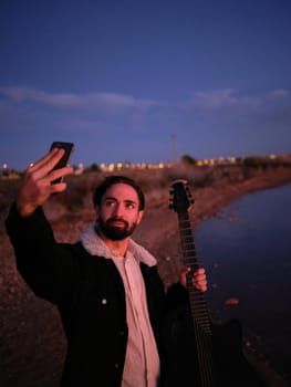 guitarist taking a selfie with his guitar on the shore of a lake, vertical close up