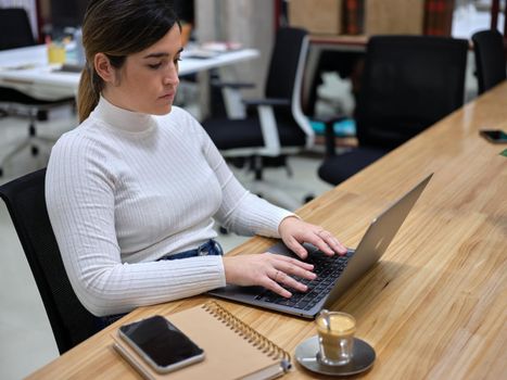 woman in a workspace using her computer with a coffee next to it, horizontal close up