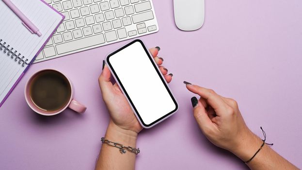 Mockup image of woman hand using a smart phone on purple background. Top view.