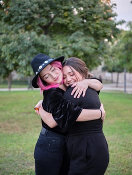 two friends in black clothes hugging each other standing in the park, vertical portrait