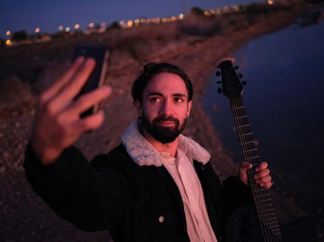 musician with his guitar snapping a selfie by a lake at dusk, horizontal photo taken from above