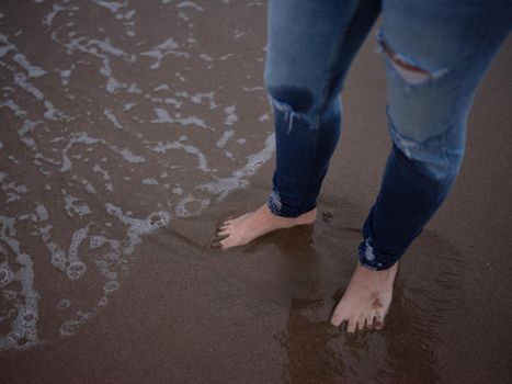 view from above of a person's legs with wet feet on the beach shore, close-up horizontal cut-out picture