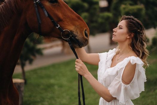 Beautiful girl in a white sundress next to a horse on an old ranch.