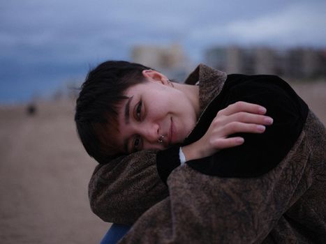 non-binary girl sitting hugging her knees and looking sideways at the camera, horizontal cutout