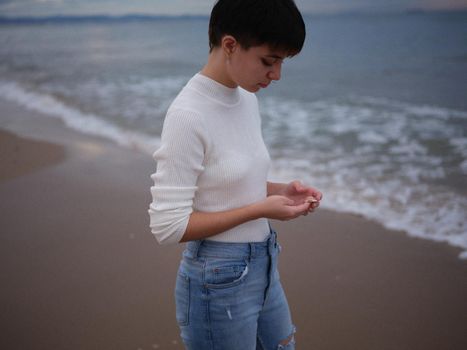 transgender on the seashore looking at a shell she is holding in her hand, horizontal close up