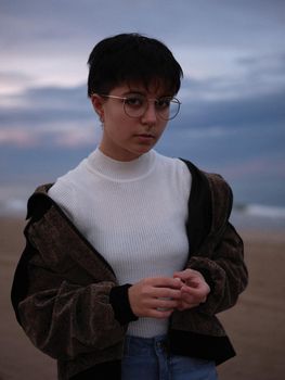 transgender woman posing in front of the beach in warm clothes and holding hands, vertical waist up portrait