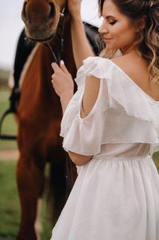 Beautiful girl in a white sundress next to a horse on an old ranch.