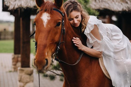 A woman in a white sundress riding a horse near a farm.