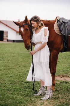 Beautiful girl in a white sundress next to a horse on an old ranch.