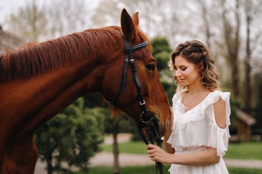 Beautiful girl in a white sundress next to a horse on an old ranch.