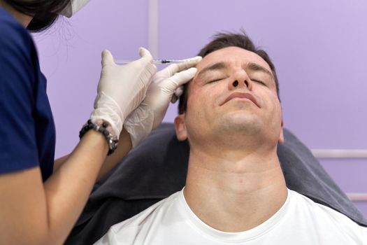 Relaxed male patient getting a botox injection into the forehead for facial rejuvenation treatment