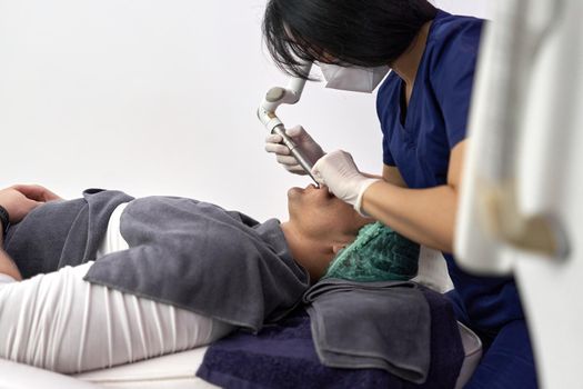Focus on a patient lying on a clinic while receiving a beauty intraoral laser treatment