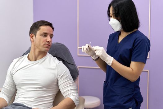 Patient sitting on a clinic and watching as a doctor prepares a Botox injection for application