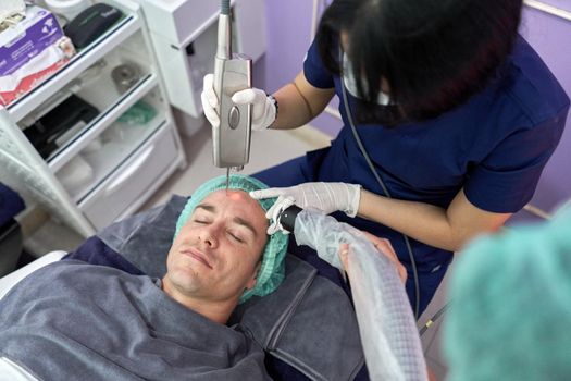 Top view of a man lying on a clinic while receiving a laser treatment to rejuvenate the skin